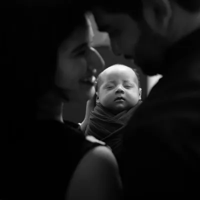 An intimate black and white portrait focusing on the tender moment between new parents and their sleeping newborn. This is pure love.
