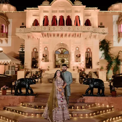 A grand portrait in front of a beautifully lit palace in Rajasthan. This shot captures the essence of a royal destination wedding, combining magnificent architecture with the couple's elegant presence.