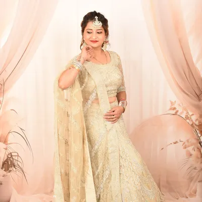 An elegant studio portrait featuring a woman in a beautiful cream-colored lehenga. The soft, draped background adds a touch of sophistication.