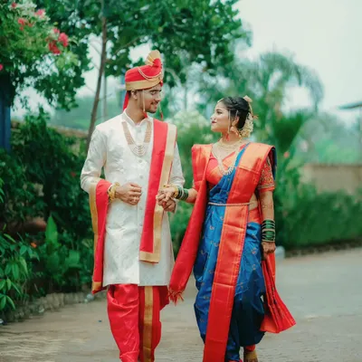 A Maharashtrian couple takes a walk together, hand in hand. The groom in his sherwani and the bride in her traditional blue and red Navvari saree create a picture of classic elegance.