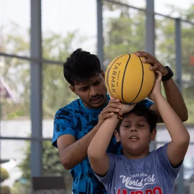 The foundation of a great player is great technique. Here, we are providing hands-on guidance to correct a young player's shooting form, ensuring he builds the right muscle memory from day one. This personal attention is key to our beginner basketball training.
