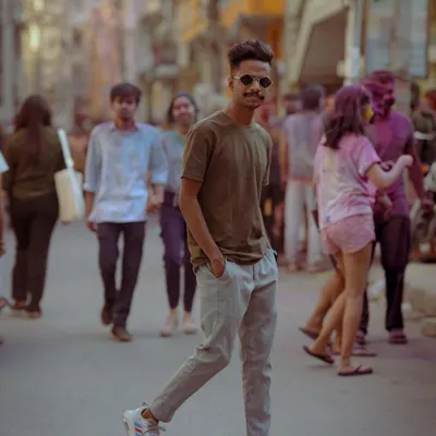 Capturing the vibe of the city streets, this portrait has a cool, candid feel. The blurred background with people celebrating Holi adds energy and context, making it a dynamic lifestyle shot.