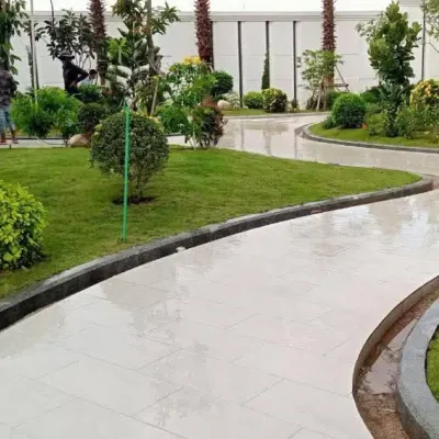 A newly installed landscape for a commercial property, featuring curving paved pathways, fresh turf, and a variety of shrubs and trees. A worker is seen giving the final touches, showcasing our hands-on approach.