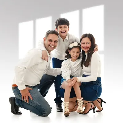 A beautiful family of four poses for a classic group portrait. The simple white background and coordinated outfits create a crisp, modern aesthetic that will never go out of style. This is a perfect example of a timeless family photograph.