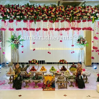 An elegant and modern Seemantha setup with a white and pink floral theme. The hanging flower strings and clean arrangement of offering plates create a sophisticated and dreamy atmosphere for the baby shower.