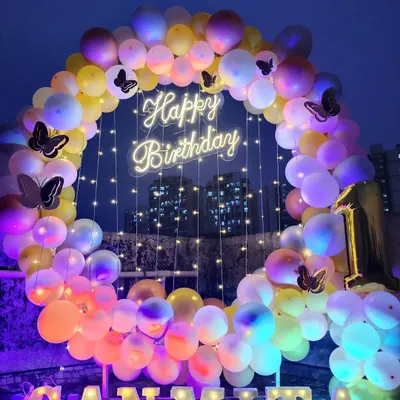 A stunning butterfly-themed birthday decoration set up on a terrace. The balloon ring with a neon sign looks beautiful against the night sky.