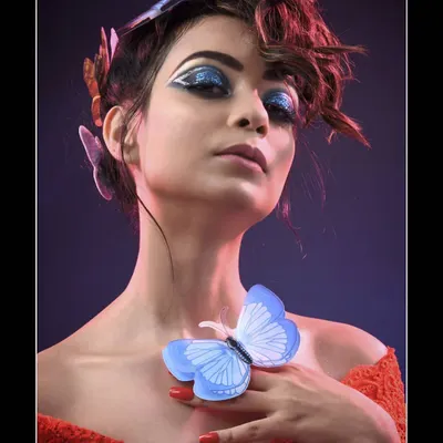 A full view of the butterfly-themed creative makeup, showing the interplay between the bold blue glitter eyeshadow and the delicate butterfly accents. The updo hairstyle was designed to keep the focus on the intricate facial details.