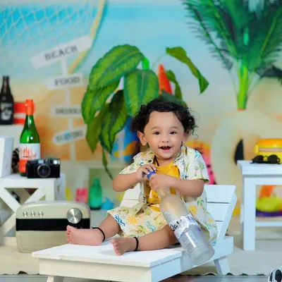 A happy baby enjoying our beach theme, complete with a miniature beach chair, surfboards, and even tiny bottles of Coca-Cola for a vintage vibe.