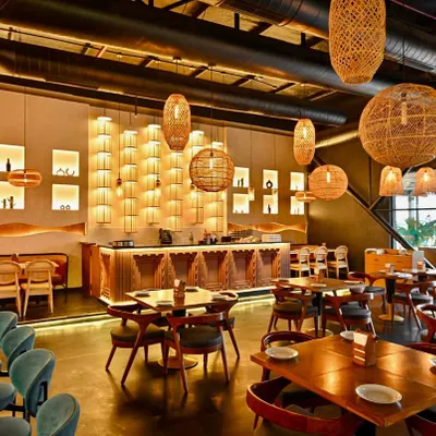 A complete view of the main dining hall at Indus Flavour, showcasing the interplay of textures and light. We used a combination of wicker pendant lights, a custom carved bar, and strategically placed spotlights to create a warm, inviting, and luxurious ambiance.