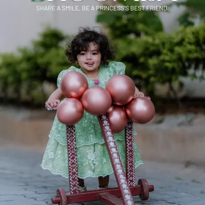 A beautiful outdoor portrait for a first birthday. Little Bhoomija looks like a princess in her lovely green dress, posing with a cute wooden walker decorated with balloons, perfectly capturing the sweetness of turning one.