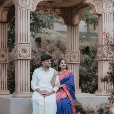 A serene pre-wedding portrait of a couple in traditional South Indian attire. The ornate stone gazebo provides a beautiful, classic backdrop that complements their outfits perfectly.