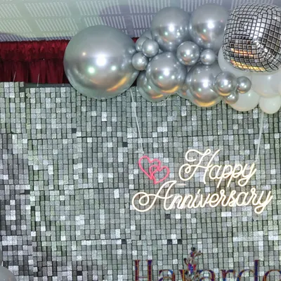 A close-up of a 'Happy Anniversary' neon sign against a silver sequin backdrop. It's a perfect, shimmery detail for a special celebration.