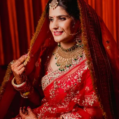 A classic portrait of a North Indian bride in her radiant red lehenga. The way she adjusts her ghunghat (veil) is a timeless pose that showcases both her traditional attire and her joyful anticipation.