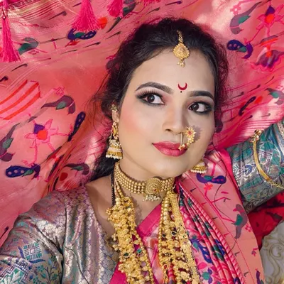 A classic Maharashtrian bride, holding the veil. The look features gold shimmery eyeshadow, winged liner, and a traditional `nath` that perfectly complements the pink Paithani saree.