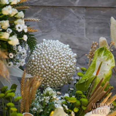 Every detail whispers elegance. Here, a sphere covered entirely in pearls sits within a lush arrangement of white and green florals, showcasing our commitment to creating unique, luxurious textures.
