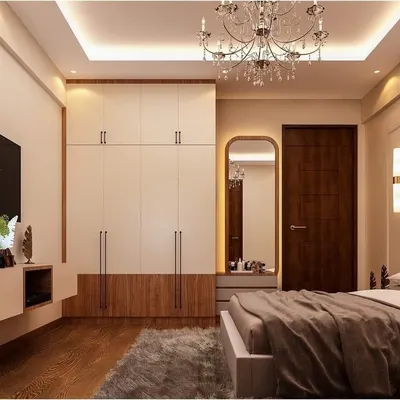 A beautifully designed bedroom that balances style and function. This space features a floor-to-ceiling wardrobe with a dual-tone wood and white finish, a dedicated dressing area with an arched mirror, and elegant chandelier lighting.