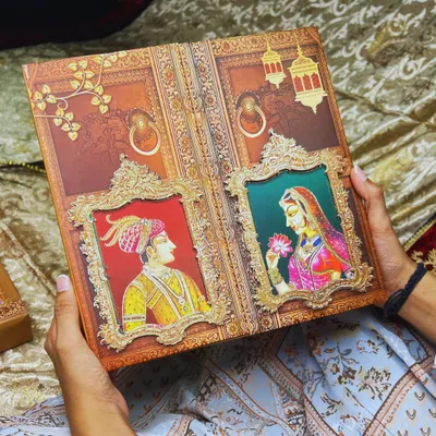 A closer look at the handcrafted Raja-Rani invitation, held to show its substantial feel and detailed artistry. This design is not just an invite, but a 'pavitra bandhan ki pehli anmol nishani' (the first precious symbol of a sacred bond).