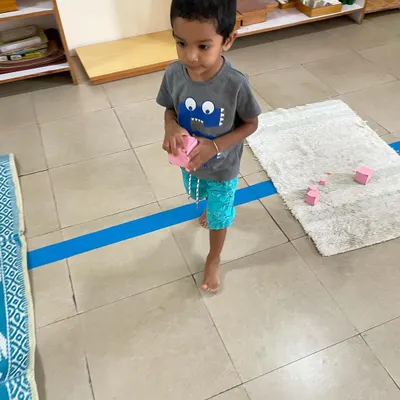 A child works with the Pink Tower, a classic sensorial material. This activity helps them visually discriminate between sizes and builds their understanding of dimensions, which is an indirect preparation for mathematics.