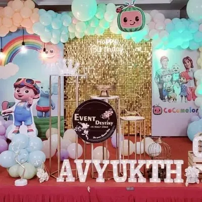 A fantastic Cocomelon theme for a first birthday party. This setup includes a gold sequin backdrop, a pastel balloon arch, and cutouts of all the favorite Cocomelon characters.
