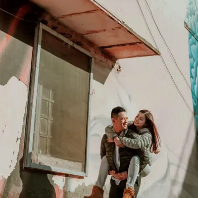 A fun and candid piggyback moment against a textured, artistic wall in the city. This shot shows how we find interesting backdrops in urban environments to tell a couple's story.