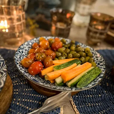 A bowl of fresh vegetables and olives, part of a festive setup for a Diwali dinner. The candlelit ambiance adds a warm and inviting glow to the dining experience.