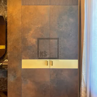 This wardrobe door features a unique ceramic-finish laminate that mimics the look of rusted or patinated metal. A horizontal band of brushed gold houses the handles, creating a striking contrast and adding a touch of luxury.