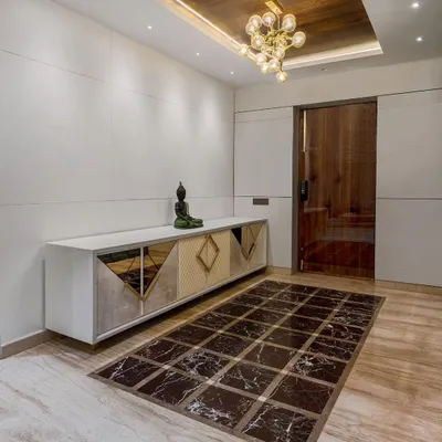 This contemporary foyer design creates a lasting first impression. A custom console with mirrored and geometric-patterned doors sits below a wooden coffered ceiling with a modern chandelier, while a marble floor inlay adds a touch of luxury.