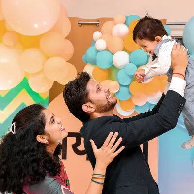A beautiful family portrait capturing a moment of pure joy. The father lifts his son, and the mother looks on with a smile, all against the backdrop of their custom-designed first birthday party.
