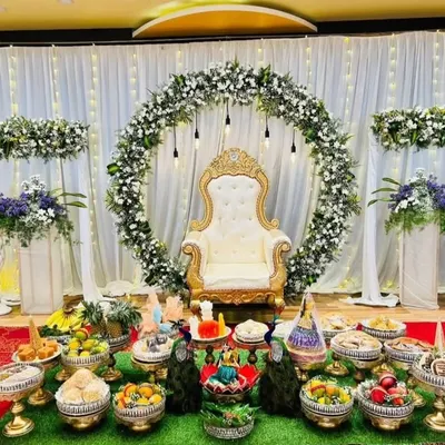 A beautiful Half-Saree ceremony stage with a white and green floral ring, a royal throne chair, and a traditional display of offerings.
