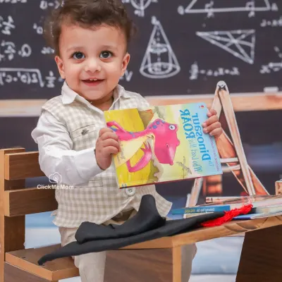 Ready to learn with a smile. This little scholar is excited for his classroom-themed photoshoot, holding up his favorite dinosaur book.
