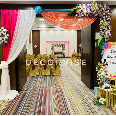 A welcoming entrance we created for a baby shower, featuring colourful drapes in pink, white, and orange, accented with fresh floral arrangements. This arch provides a beautiful first impression and a glimpse of the main decor inside.