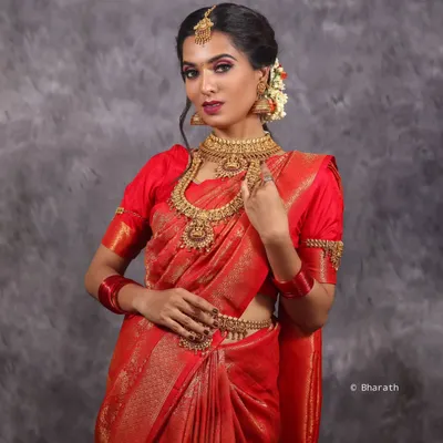 A stunning studio portrait of a model in a traditional red silk saree and temple jewelry, perfect for a bridal or festive look.