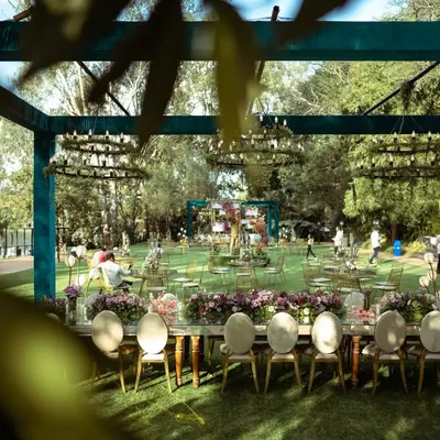 A beautiful long shot of the lakeside reception setup. The open-sided structure, adorned with greenery chandeliers, allowed guests to dine while enjoying the stunning natural surroundings.
