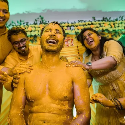 The very definition of a joyful Haldi. The groom is laughing uncontrollably as his friends and family playfully smear him with turmeric paste.