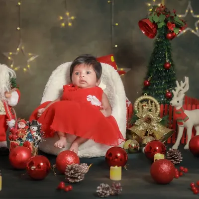 Baby's first Christmas! This little one is sitting so sweetly in her festive red dress, surrounded by all the magic of the season.