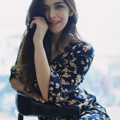 A relaxed portrait of a woman in a floral dress, seated by a window. Her warm smile and direct eye contact create an inviting and confident image, showcasing how natural light can be used to create beautiful, soft-lit fashion shots.