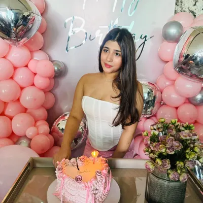 A perfect birthday moment. The birthday girl with her cake, set against the pink and silver backdrop we designed. The setup includes a custom 'Happy Birthday' sign and fresh flowers to complete the celebratory feel.