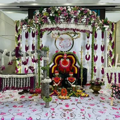 This is a complete view of a traditional naming ceremony setup for baby Vihaa. It includes a silver-plated cradle and a backdrop with deity arrangements, all adorned with fresh flower garlands and traditional elements.
