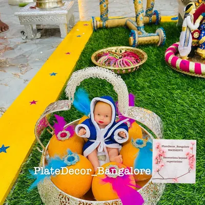 A baby boy themed platter for a seemantham ceremony. The basket contains decorated oranges and a cute baby doll dressed in a blue robe, accented with blue and pink feathers.