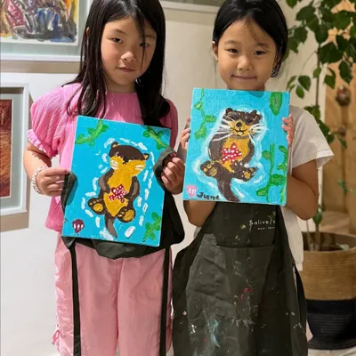 Two young artists proudly holding up their adorable otter paintings. It's wonderful to see them bring their ideas to life with acrylics on canvas during our guided sessions.