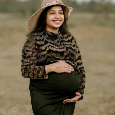 A solo maternity portrait capturing the pure happiness of a mother-to-be. Her joyful smile and the natural, open field setting create a sense of peace and contentment. The simple hat adds a touch of timeless style.
