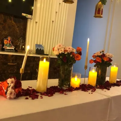 An intimate table setup for a romantic dinner, featuring multiple candles, fresh flower bouquets, and scattered rose petals.