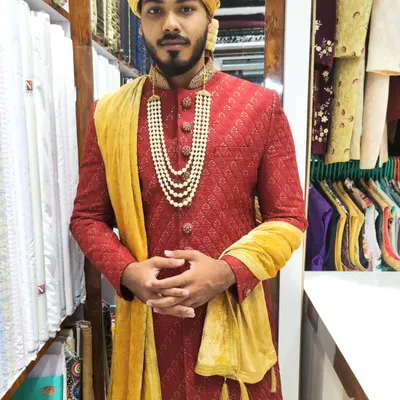 A classic red and gold combination for the groom. This textured red sherwani is paired with a gold turban and a velvet stole for a truly traditional and royal wedding look.