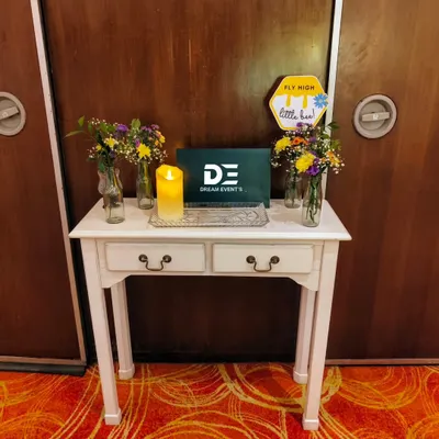 A charming welcome table setup for a first birthday party, featuring a small easel, fresh flower vases, and a candle to greet guests.