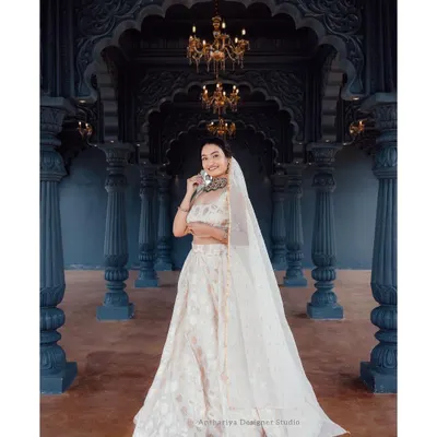 This full-length view shows the grandeur of our off-white brocade lehenga. Set against a regal backdrop, this outfit is a perfect rental choice for a bride's reception or a formal evening event.