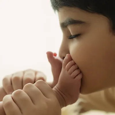 The beginning of a lifelong bond. An older brother gently kisses his newborn sibling's tiny foot, a moment of pure, unscripted love.