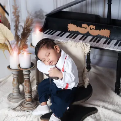 Dressed in a tiny shirt and suspenders, this baby boy dozes peacefully while leaning against the piano stool. It's a charming and creative pose that adds a story to the portrait.