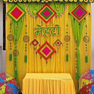 A classic Mehendi ceremony backdrop with bright yellow and green drapes, colorful hangings, and traditional umbrellas.