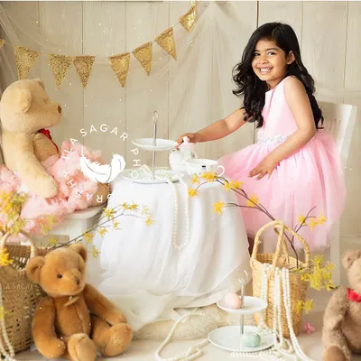 A whimsical toddler portrait session. This little girl is enjoying a make-believe tea party with her teddy bear, her bright smile showing how much fun she's having.