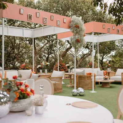 A modern and chic outdoor lounge setup for a daytime wedding ceremony, featuring clean lines, comfortable seating, and personalized photo frames on the canopy.